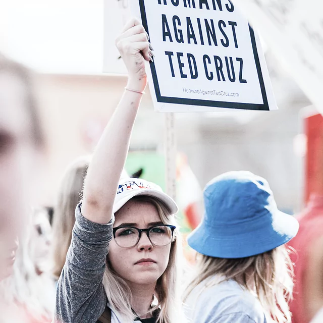 A woman holds a sign reading "Women Against Ted Cruz" at a protest, expressing her political stance.