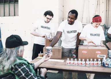 Volunteers distribute food to individuals at a table during a community outreach event.