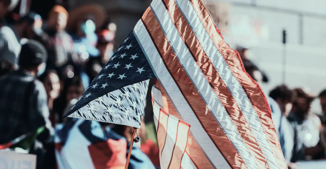 A large American flag is being held aloft by a diverse crowd of people