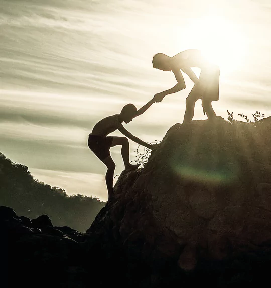 Two people helping one another ascend a rock