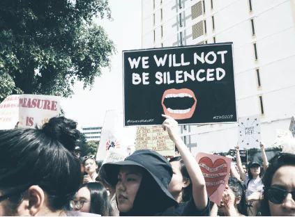 A diverse crowd of people holding signs that read "We will not be silent,"